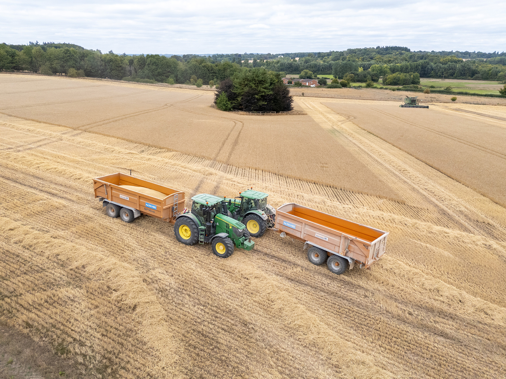 Two Richard Western SF16HS Grain Trailers hitched to John Deere tractors, parked on the headland of a wheat field